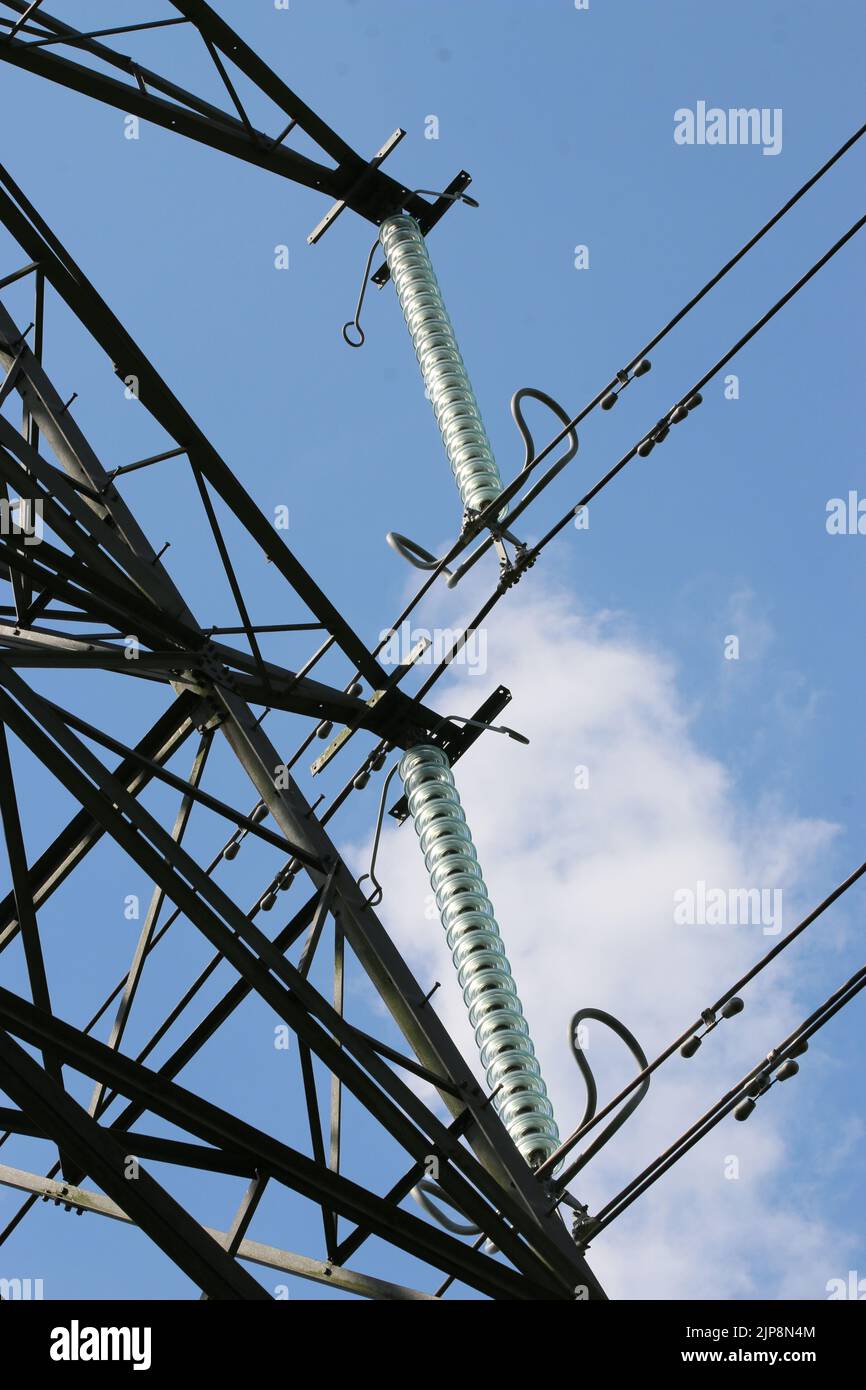 Electricity pylon with high voltage cables in close up with a background of blue sky with white clouds. Stock Photo
