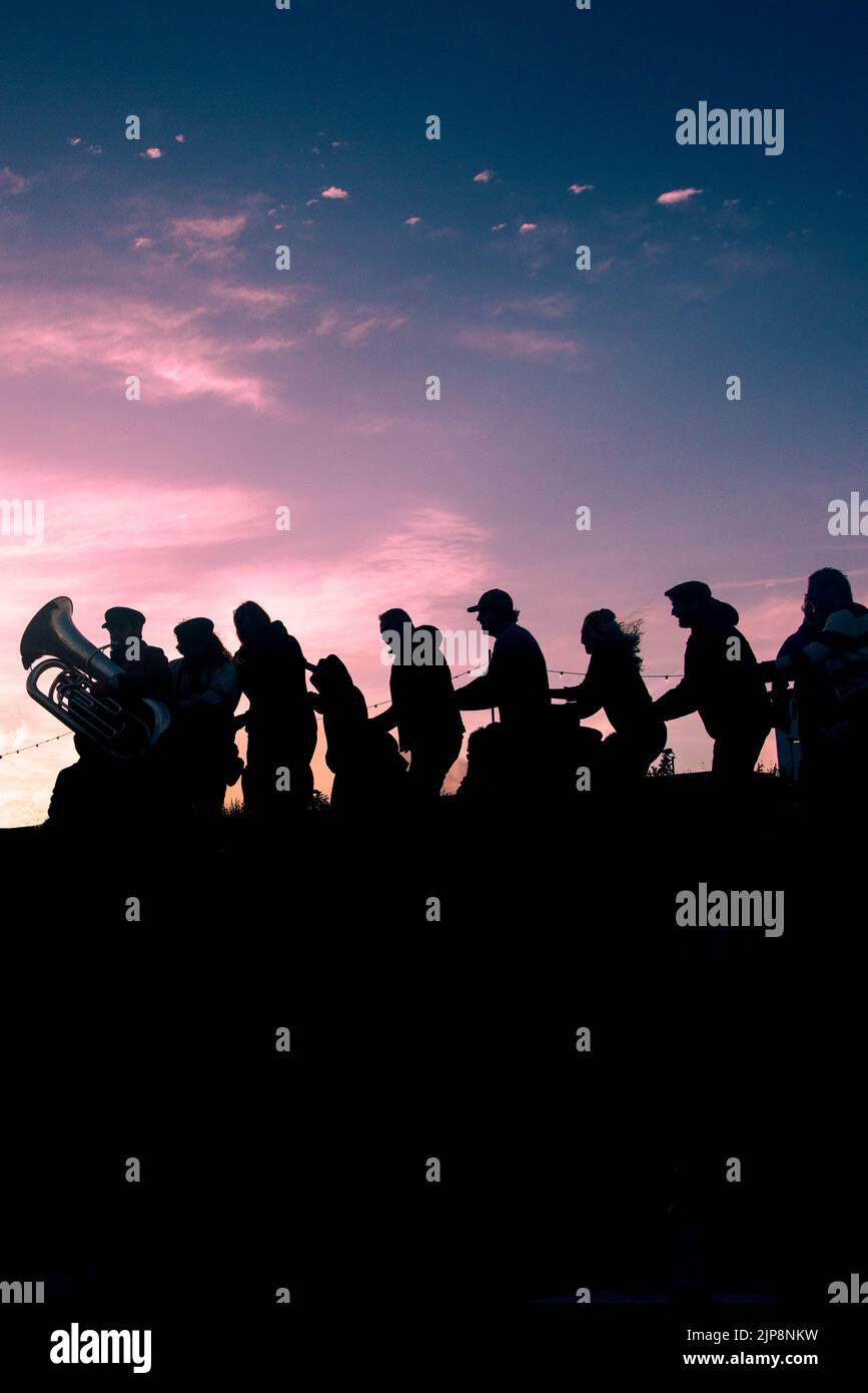 The silhouette of people forming a conga line with musicians from iThe Old Time Sailors performing at the Newquay Orchard amphitheatre in Cornwall. Stock Photo