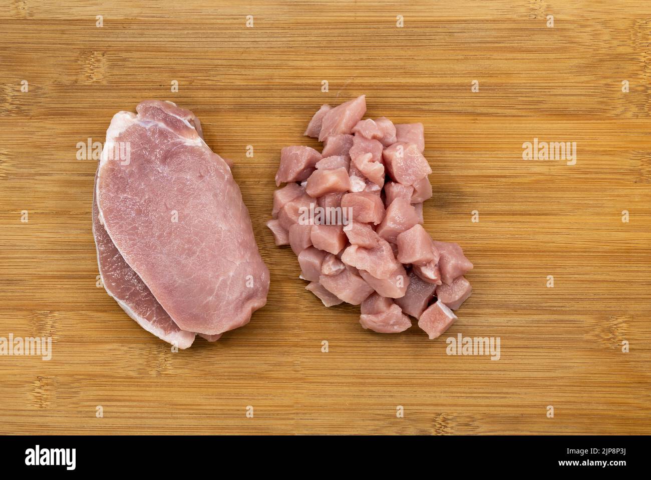 Top view fresh pork fillet and pile of cube cut pork on bamboo wooden board. Two different styles of the cut of fresh pork meat. Stock Photo