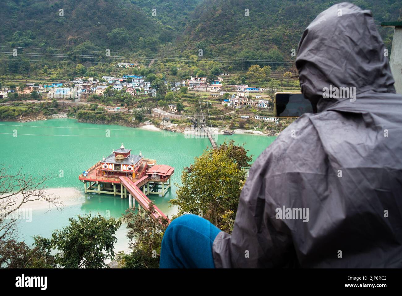 January 24th 2022, Srinagar Uttarakhand India. A male tourist with a backpack taking a photograph of Dhari Devi hinduTemple located on the banks of Al Stock Photo