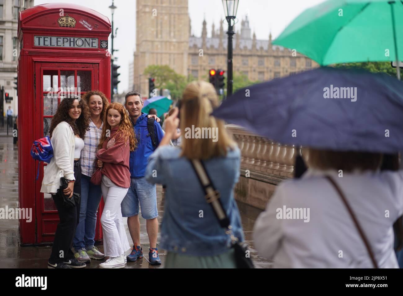 Tourists pose for a photograph beside a traditional red telephone box as rain falls in Westminster, central London. Yellow weather warnings are in place for most of the UK on Tuesday after weeks of little rain and warm conditions have caused droughts, leaving land parched. Picture date: Tuesday August 16, 2022. Stock Photo