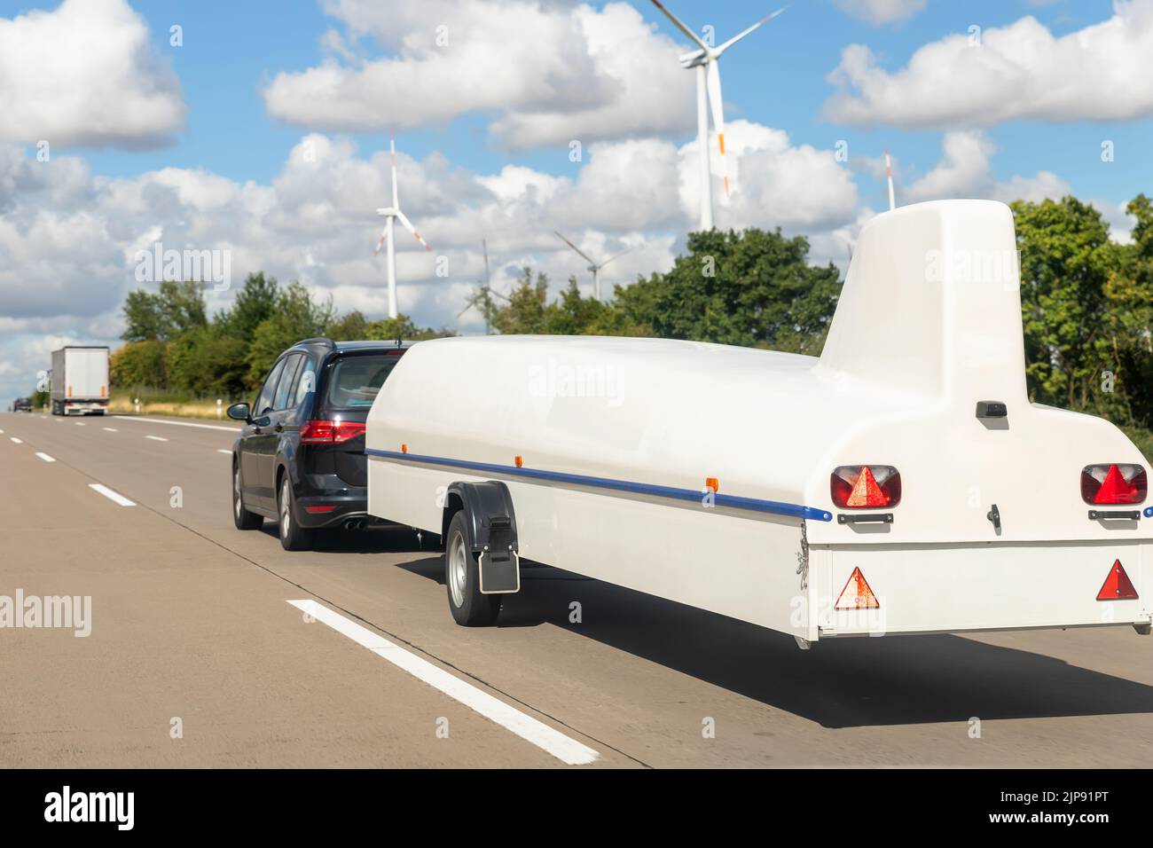 Big white disassembled glider plane in cover box on trailer towed by van or suv on highweay road sunny day against blue sky. Sailplane equipment Stock Photo