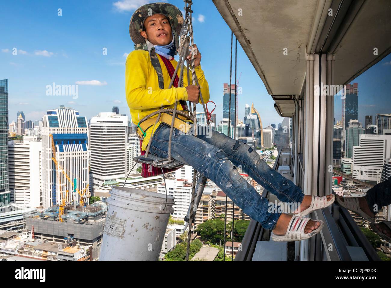 Thai worker using Bosun Chair to repair skyscraper, abseiling above Bangkok, Thailand Stock Photo