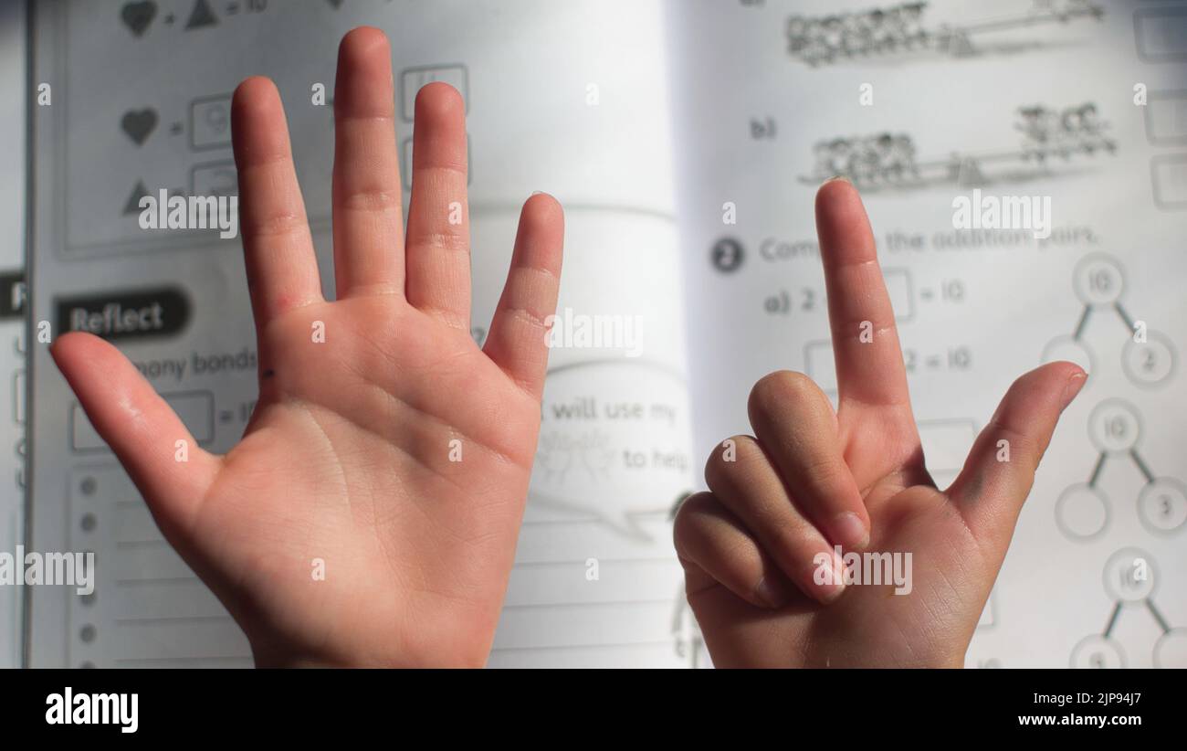 A closeup shot of a child counting with their fingers and doing their maths homework Stock Photo