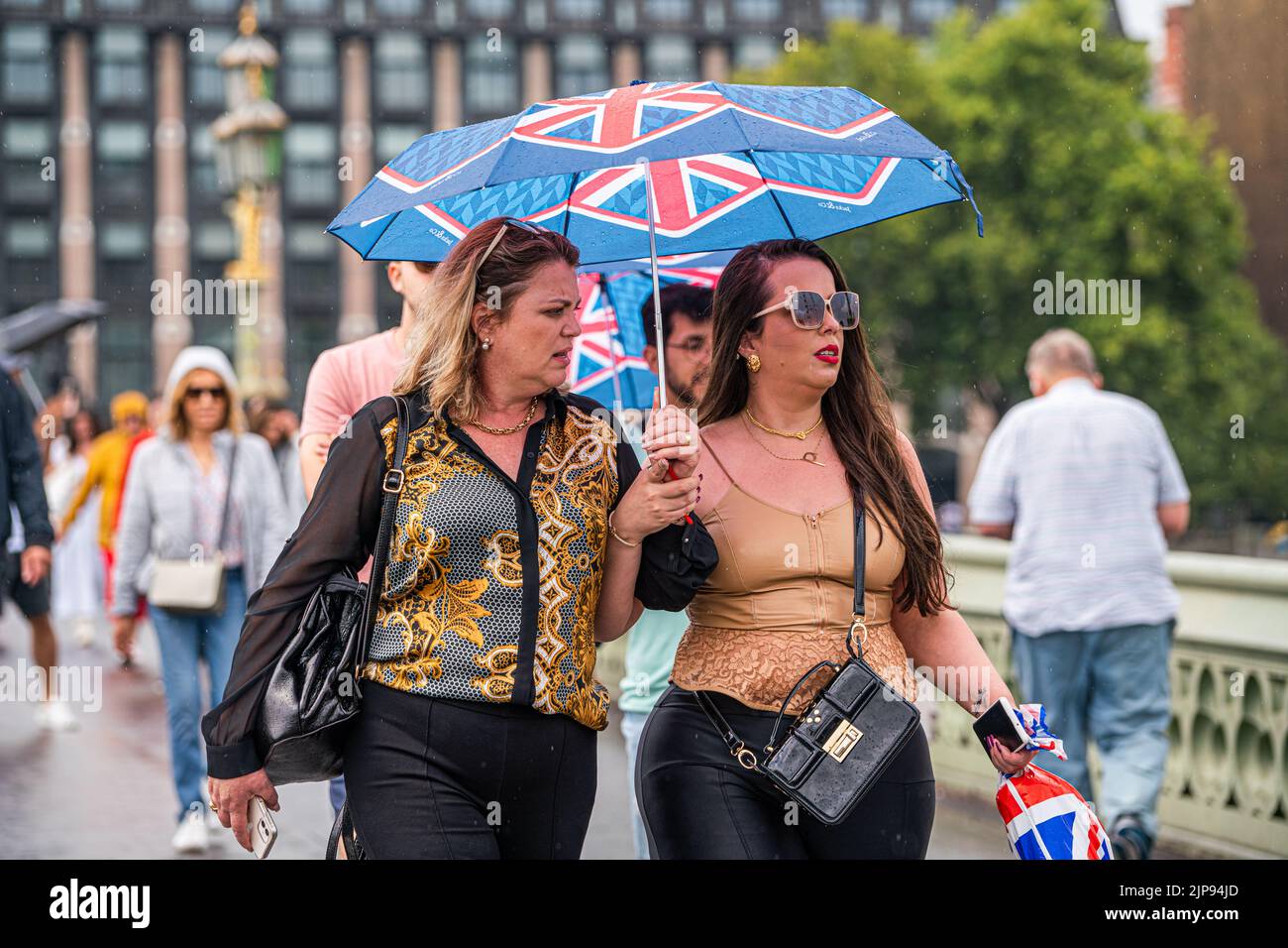 Westminster London, UK. 16 August 2022 . Pedestrians walk underneath an Union Jack umbrella on Westminster bridge during rain showers as the drought ends  after the prolonged dry spell and the driest summer in 46 years as the met office issues a yellow warning for thunderstorms and flash floods . Credit. amer ghazzal/Alamy Live News Stock Photo