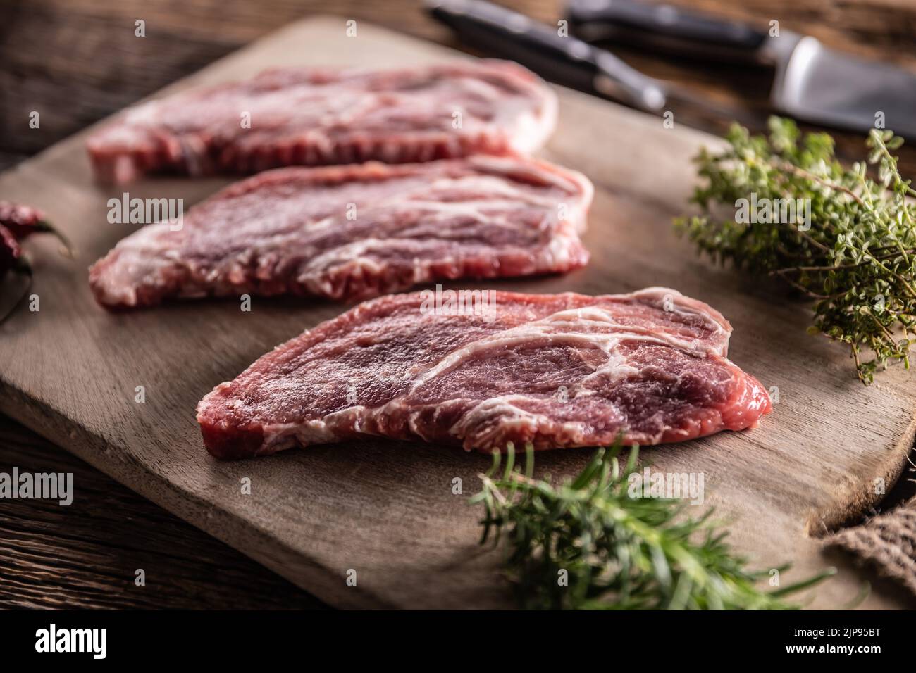 Raw pork neck cut on a cutting board with rosemary and thyme herbs. Stock Photo