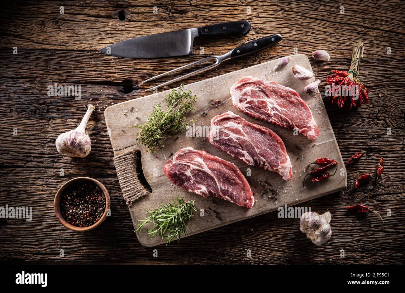 Three sliced pieces of pork neck with herbs, chili spices and garlic on a cutting board. Stock Photo