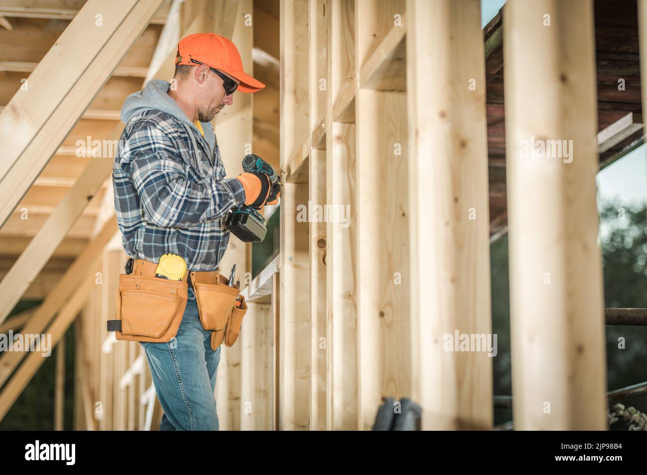 Caucasian Middle Aged Construction Worker Wearing Leather Tool Belt Holding Electric Screwdriver in His Hands Ready to Start Working on Wooden Skeleto Stock Photo