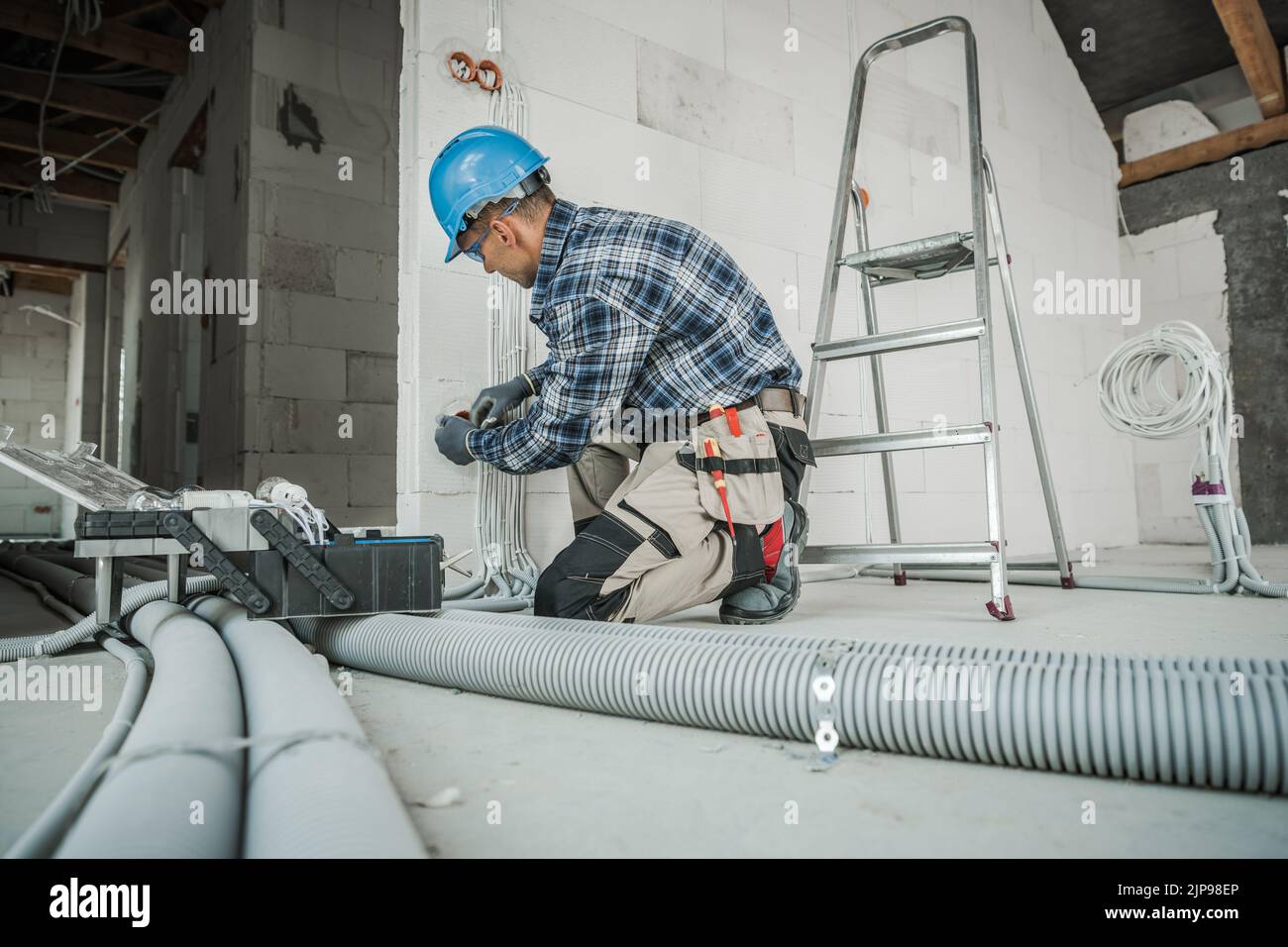Professional Electrical Installation Worker in Blue Hard Hat Working with Power Line Inside Newly Built Residential Building. Construction Site in the Stock Photo