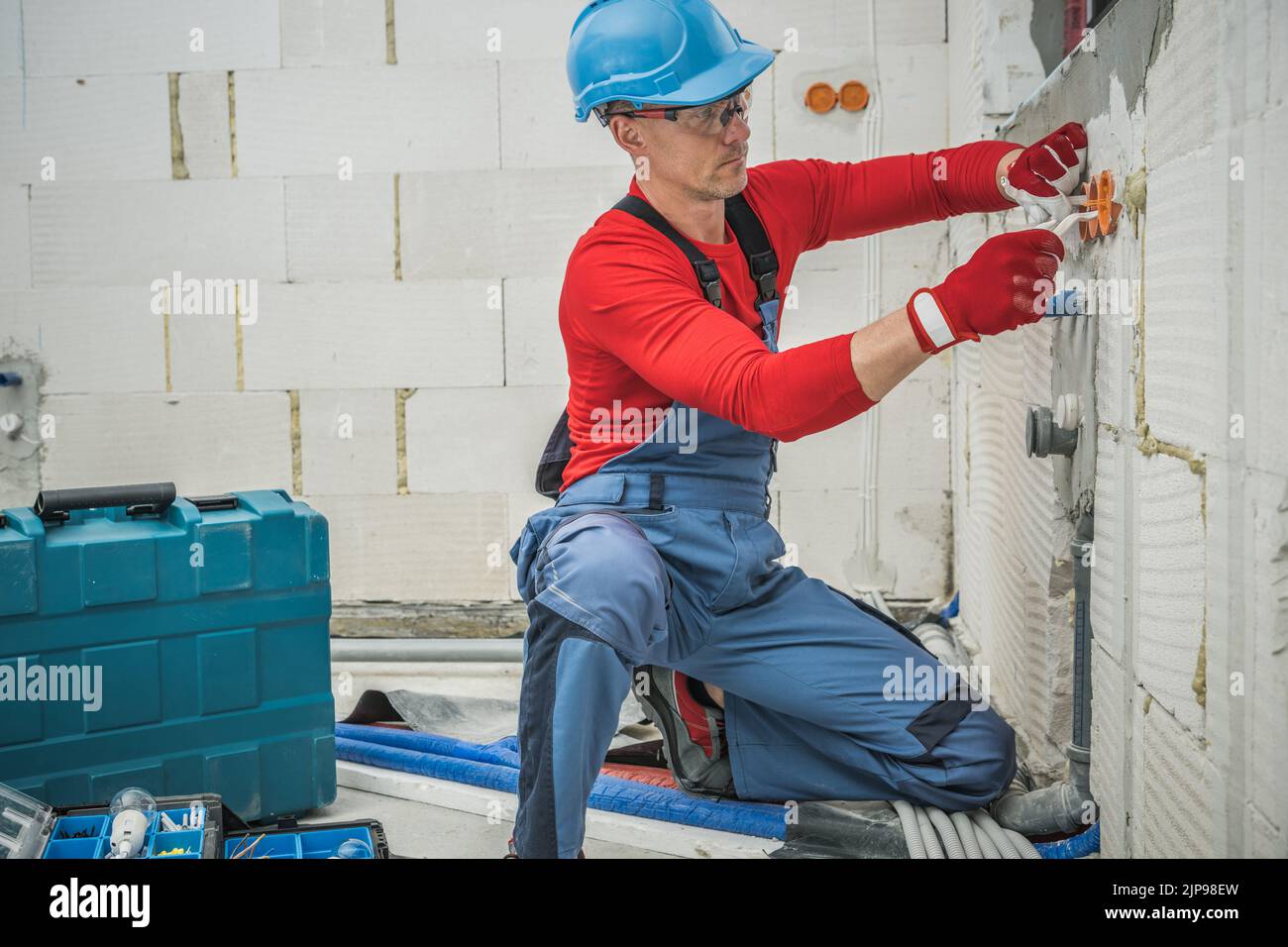 Installation of Electrical System in Freshly Build Residential House. Caucasian Worker Fitting Power Sockets in the Wall. Industrial Theme. Stock Photo