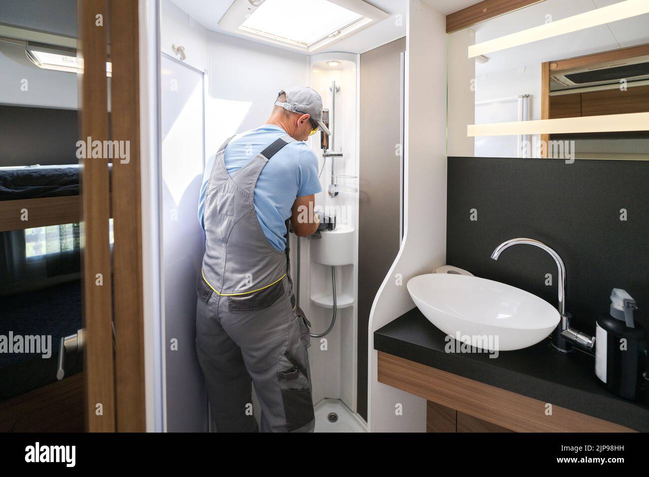 Rear View of Caucasian Worker in Grey Uniform Repairing the Hand Shower in Recreational Vehicle Bathroom. RV Care and Maintenance Theme. Stock Photo
