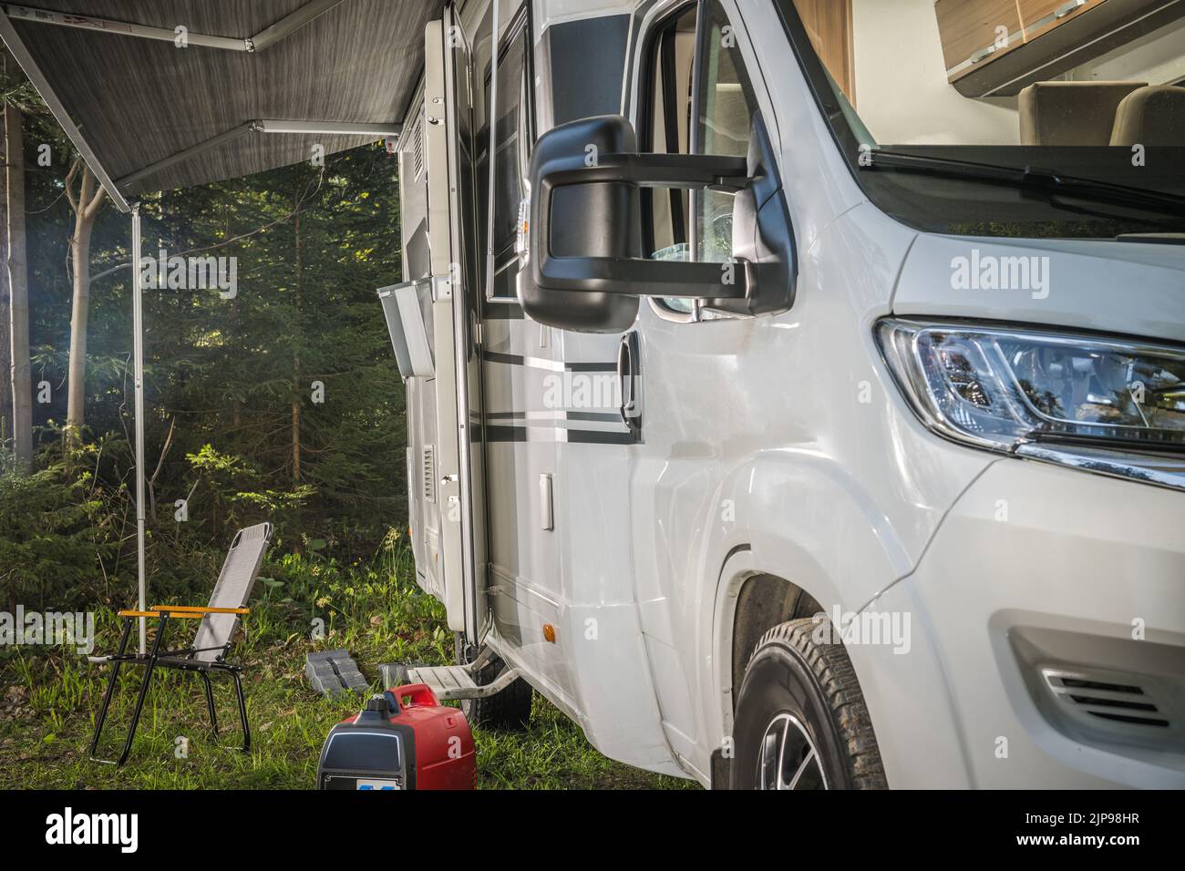 Closeup of Modern White Camper Van Parked in the Middle of Green Woods for a Night Stopover. Motorhome Traveling Theme. Stock Photo