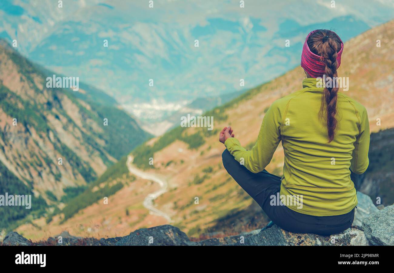 Rear View of Female Hiker Sitting on the Mountain Trail Meditating with a Scenic View in Front of Her. Hiking and Trekking Enthusiast. Travel and Adve Stock Photo