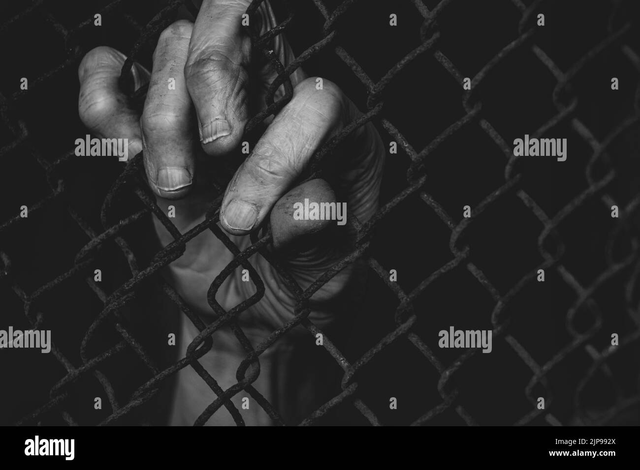 Old female hands hold on to a rusty fence in the dark, Ukrainian prisoners in the war in Ukraine, stop the war 2022 Stock Photo