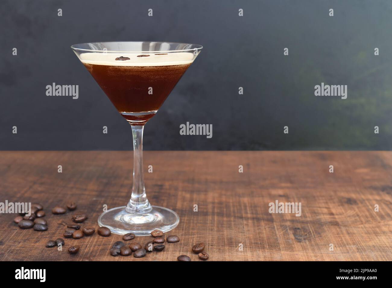 Glass of espresso martini with coffee beans on wooden table and black