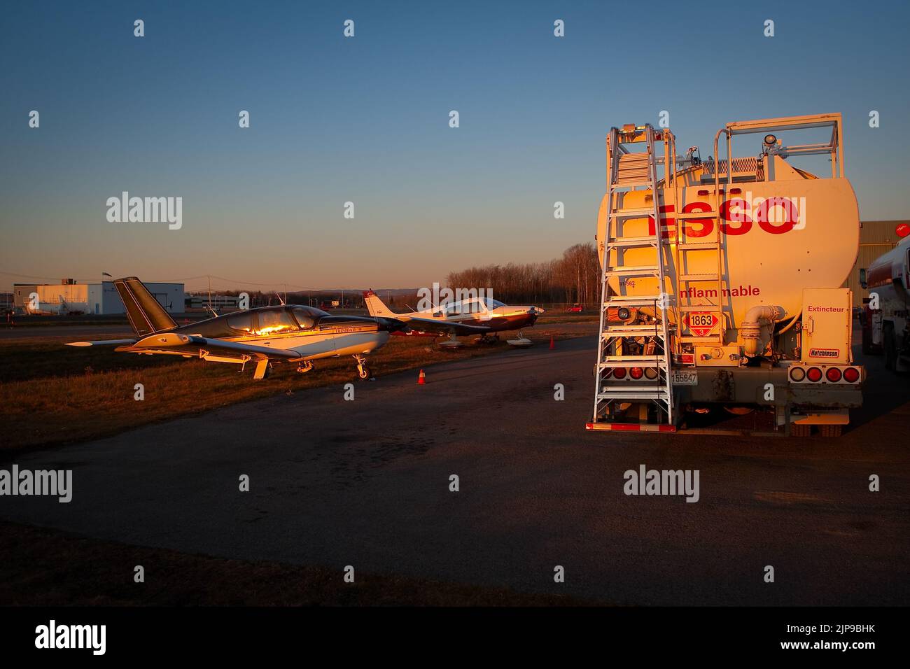 The sun set on a Esso oil truck and two small aircraft at the Quebec City Jean Lesage International Airport, also known as Jean Lesage International Airport (French: Aeroport international Jean-Lesage de Quebec, or Aeroport de Quebec) (IATA: YQB, ICAO: CYQB) November 11, 2009. Stock Photo