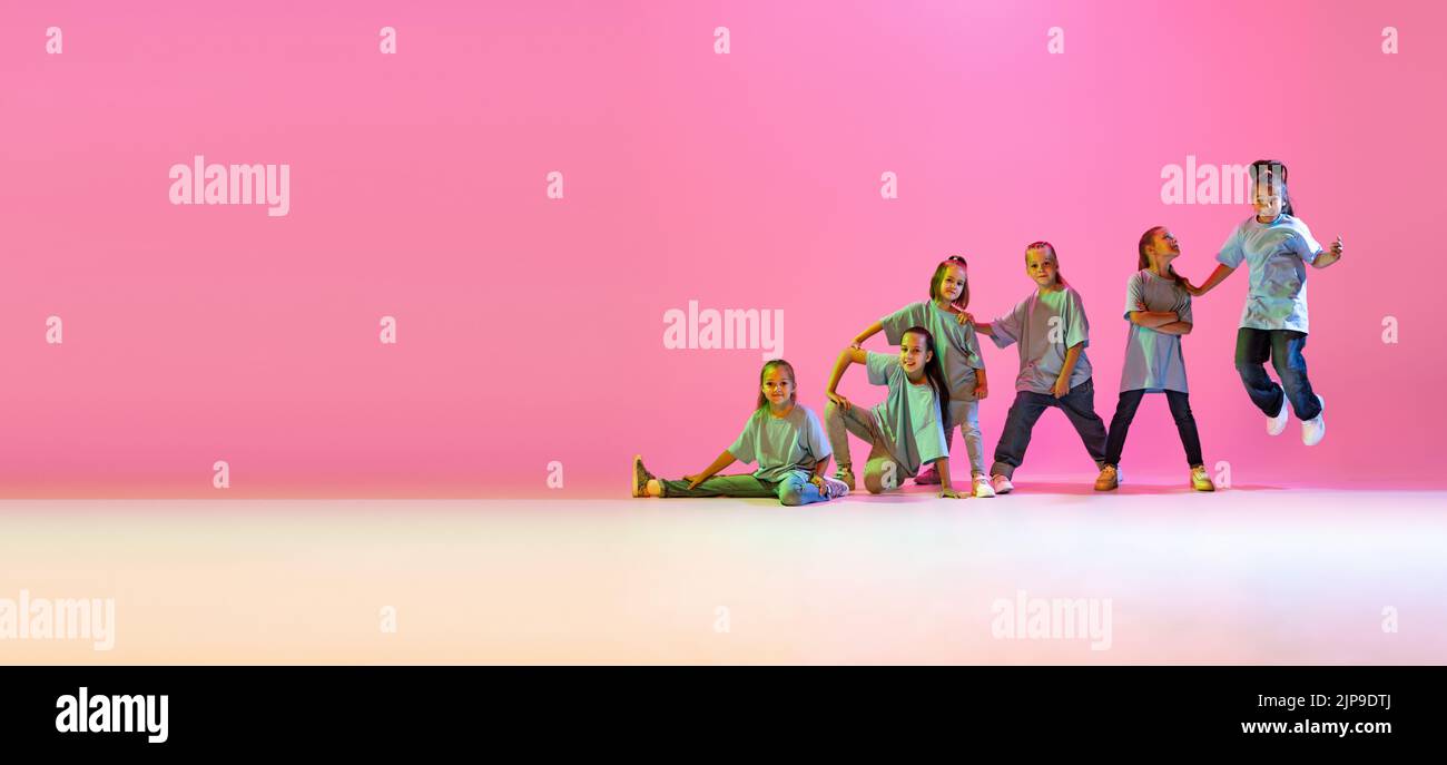 Dance group of happy, active little girls in t-shirts and jeans in action isolated on orange background in neon. Concept of music, fashion, art Stock Photo