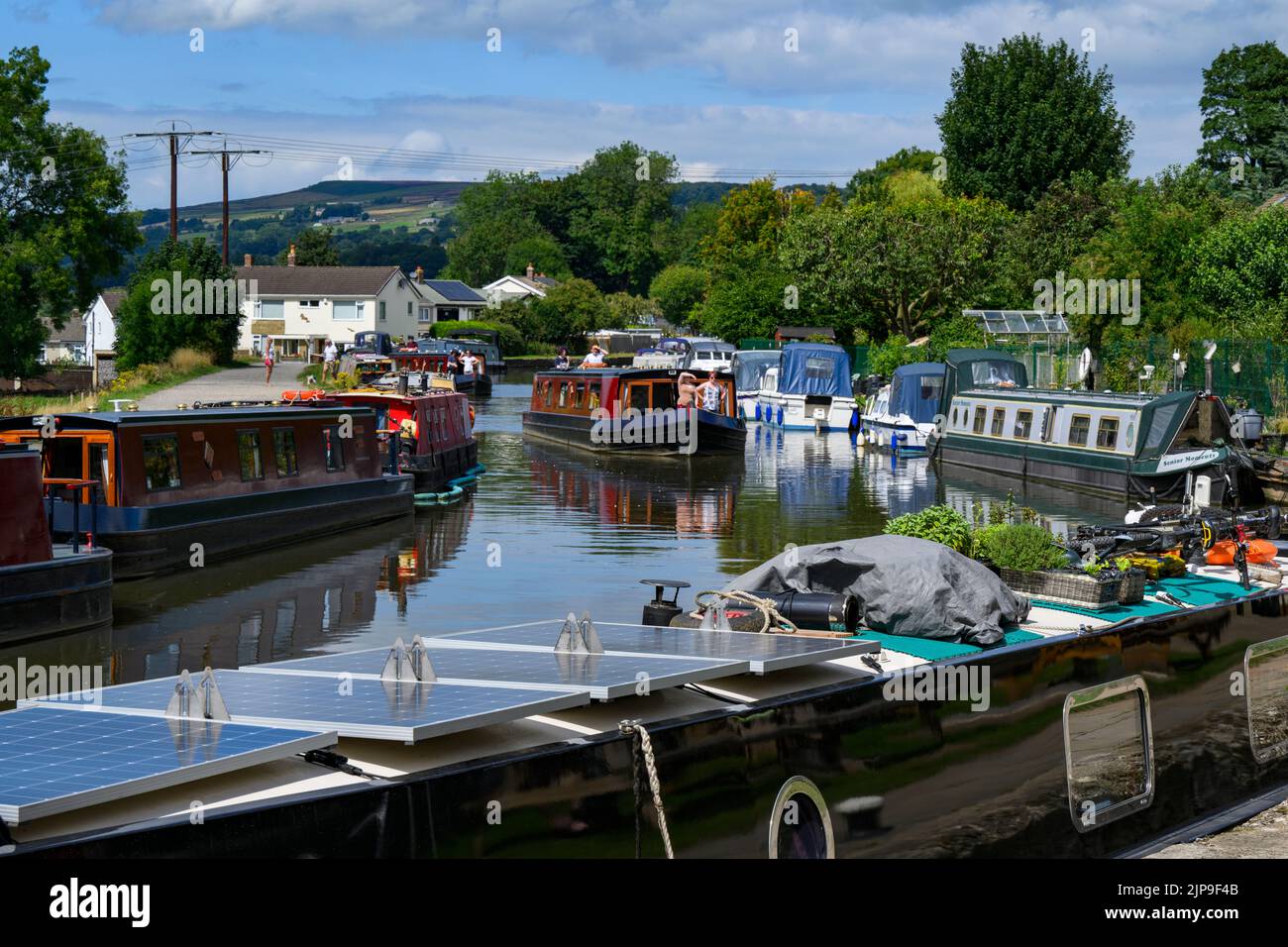 Barges at busy moorings, self-drive hire boat traveling, scenic sunny stretch of Leeds Liverpool Canal & towpath - Bingley, West Yorkshire England UK. Stock Photo