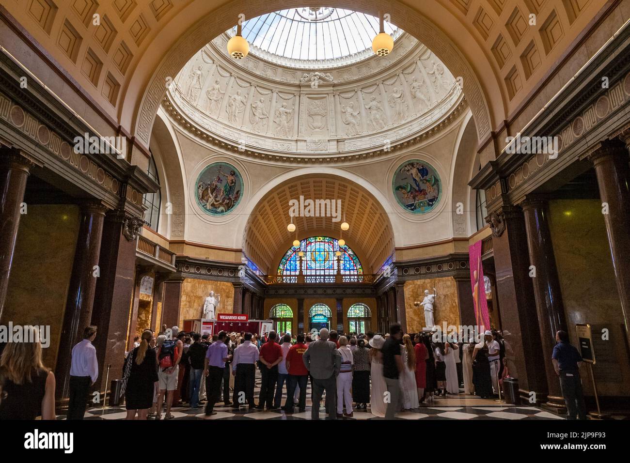 Great view inside the Wiesbaden's Kurhaus (spa house) in Germany. People gathered in the foyer, under the dome, supported by piers with white statues... Stock Photo