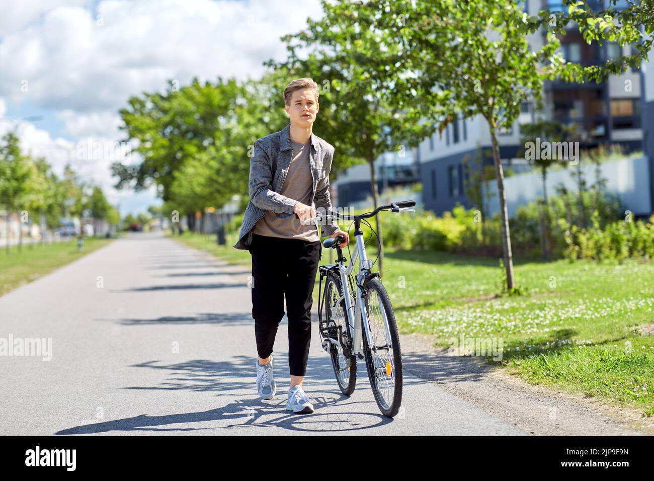 young man with bicycle walking along city street Stock Photo