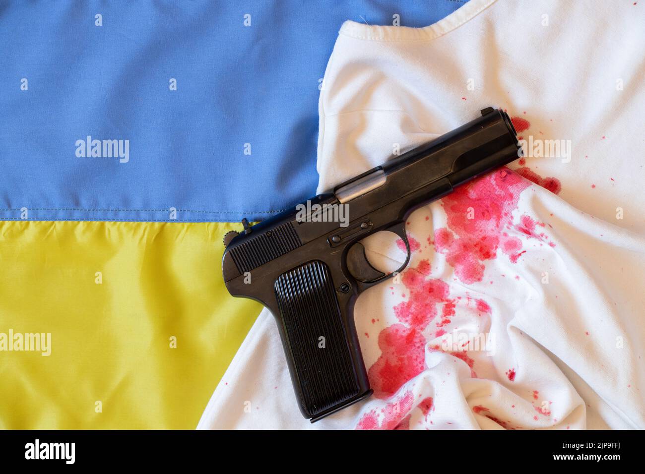 The gun lies on a bloody female dress on the flag of Ukraine, war in Ukraine, weapons, violence against Ukrainians 2022 Stock Photo
