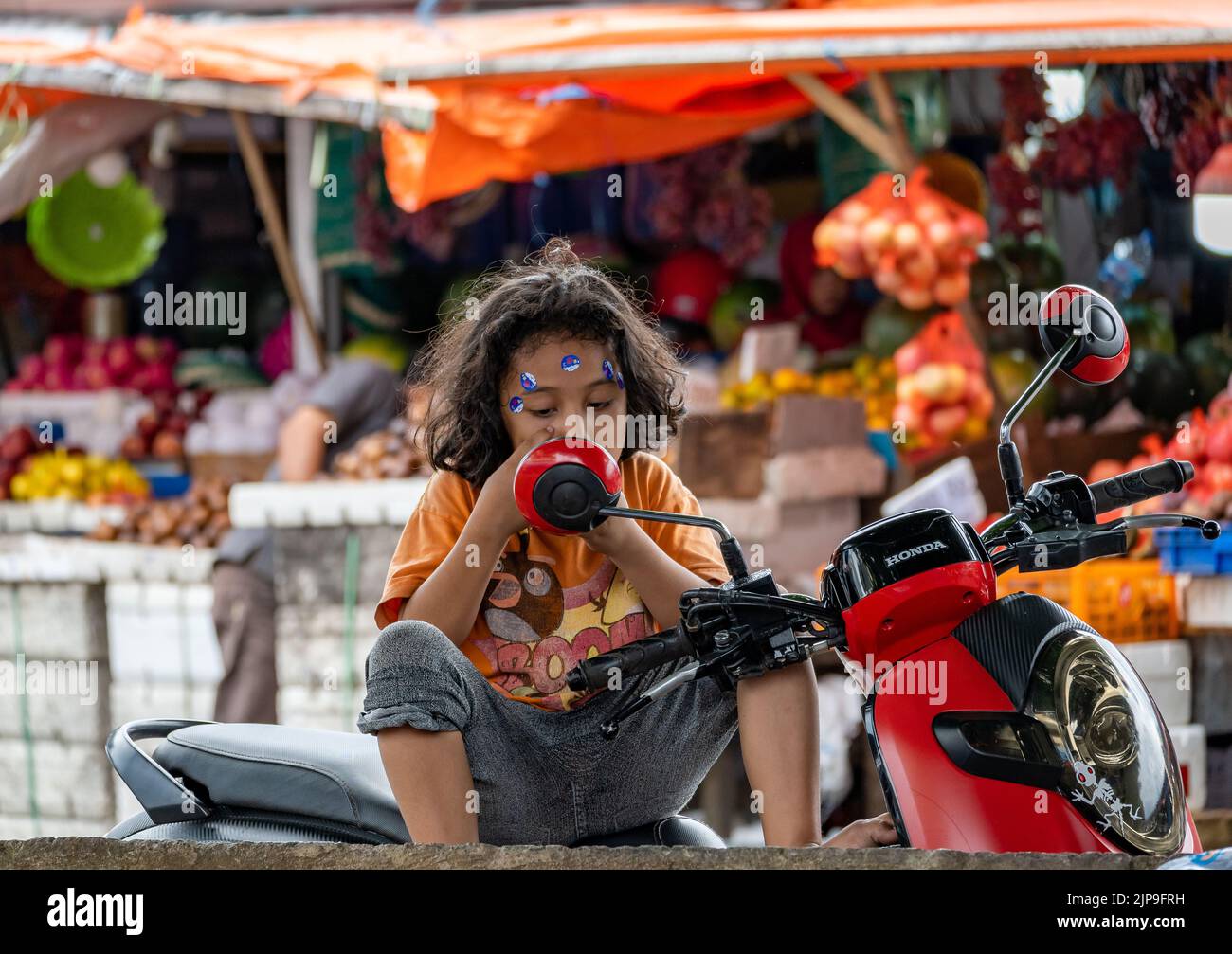 A young local girl looking at the mirror of a motorbike. Ternate, Indonesia. Stock Photo