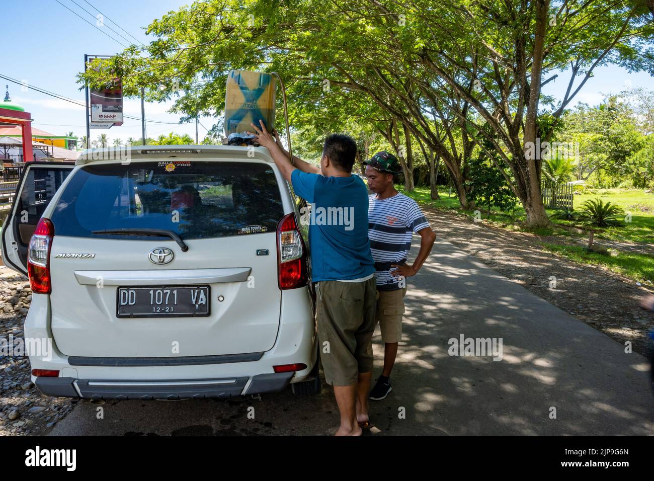 Two men fill up a car with gasoline from a plastic jug. Halmahera, Indonesia. Stock Photo