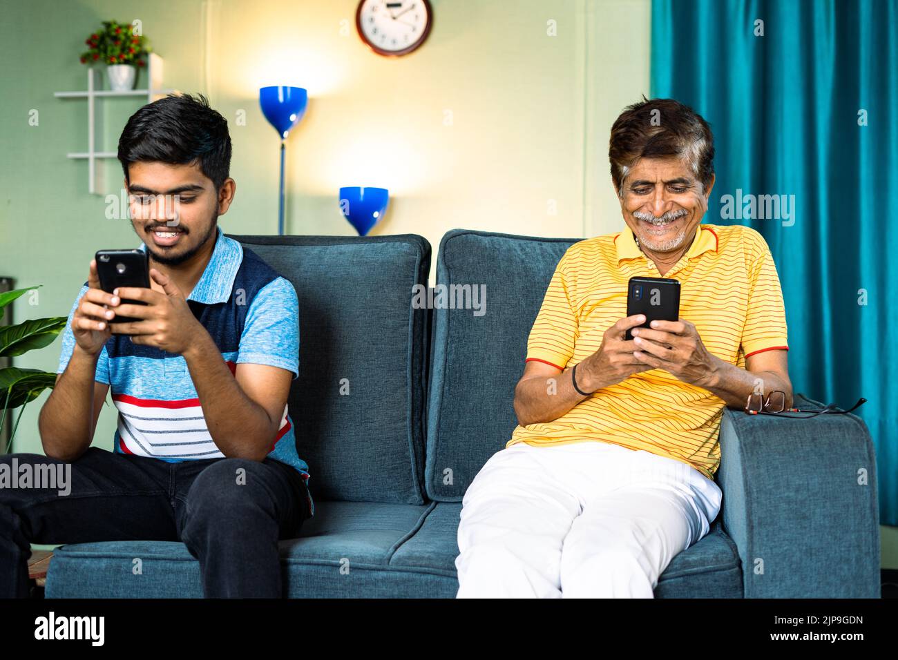 Focus on father, father and son busy using smartphone while sitting on sofa in distance at home - concept of Mobile phone addiction, digital Stock Photo