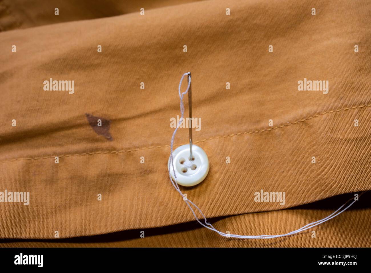 sewing on a button with a sewing needle and thread Stock Photo - Alamy