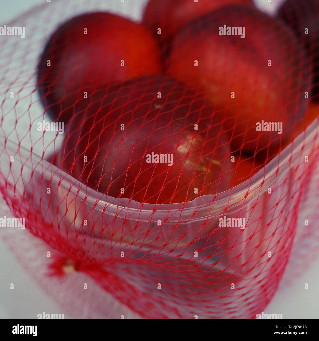 Nectarines in a  plastic box with a net. Supermarket packaging. Too much plastic waste is produced. Stock Photo