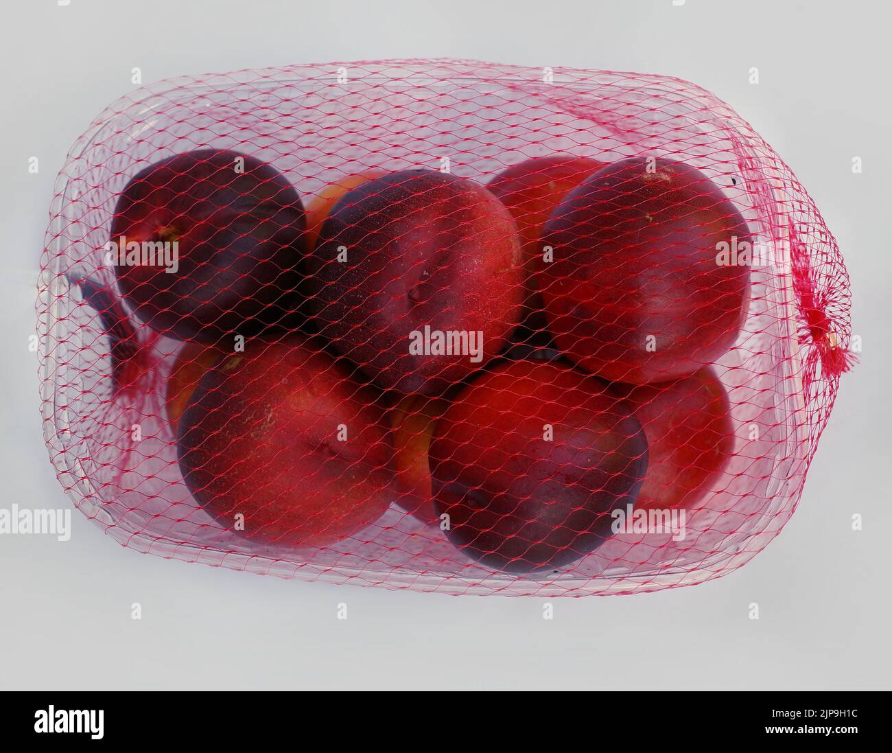 Nectarines in a  plastic box with a net. Supermarket packaging. Too much plastic waste is produced. Stock Photo