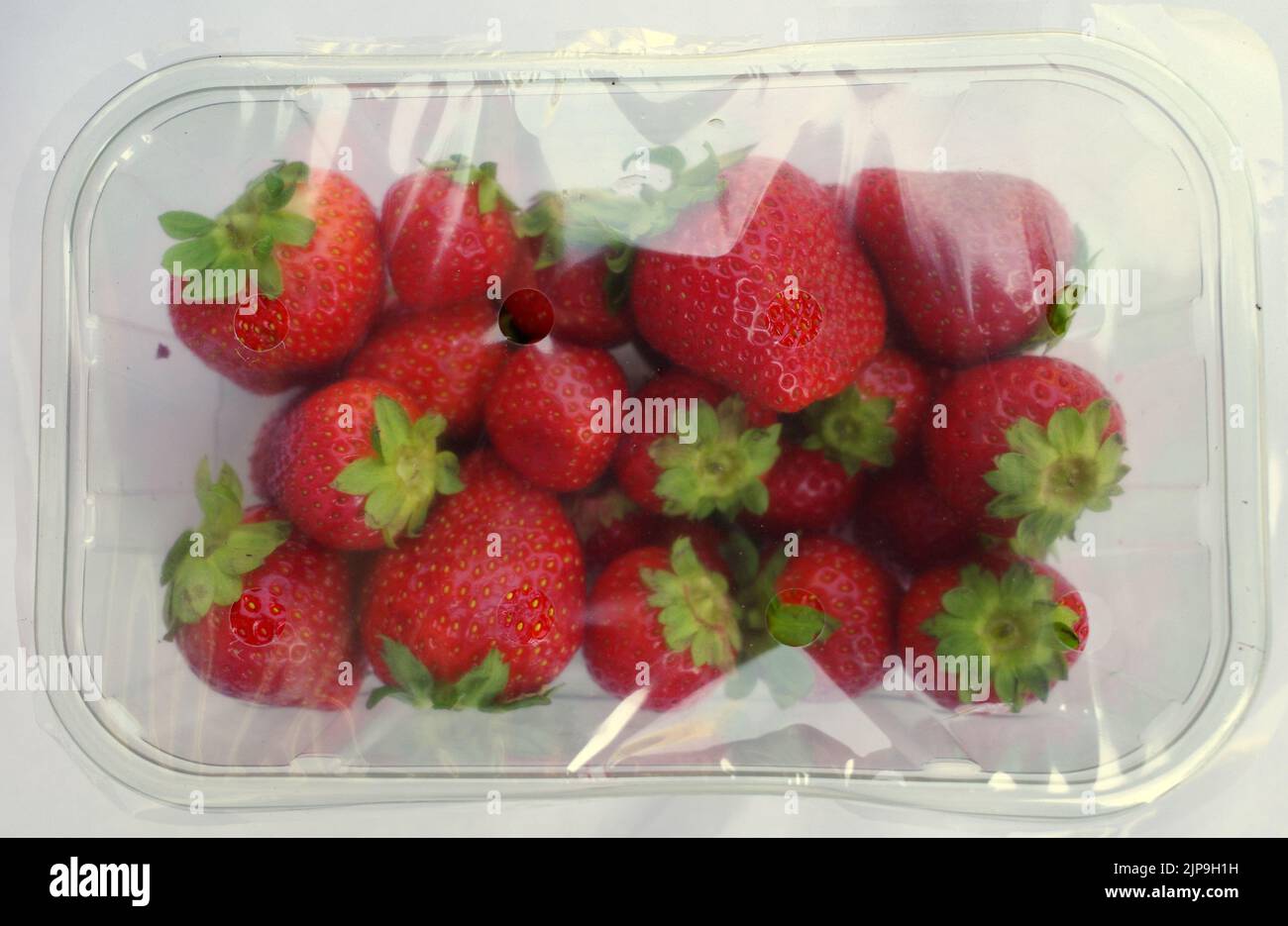 Strawberries in a sealed plastic box. Supermarket packaging. Too much