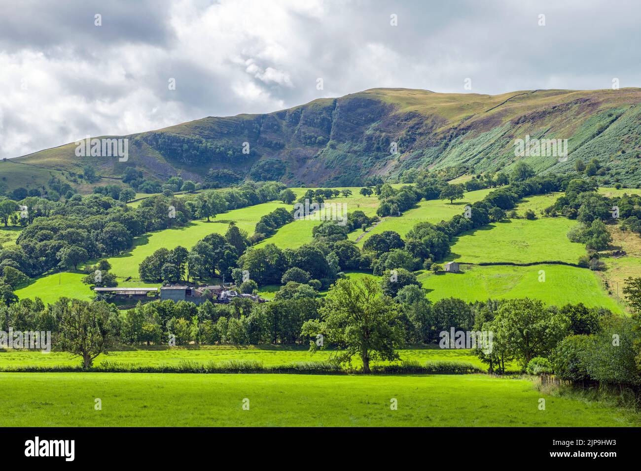 A stunning landscape view of both farmland and a high rocky fell as you head out west towards Sedbergh along Dentdale Stock Photo
