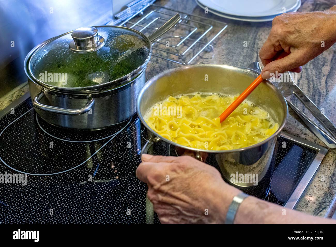 close-up of old womans hands and stove with a pot and pasta Stock Photo