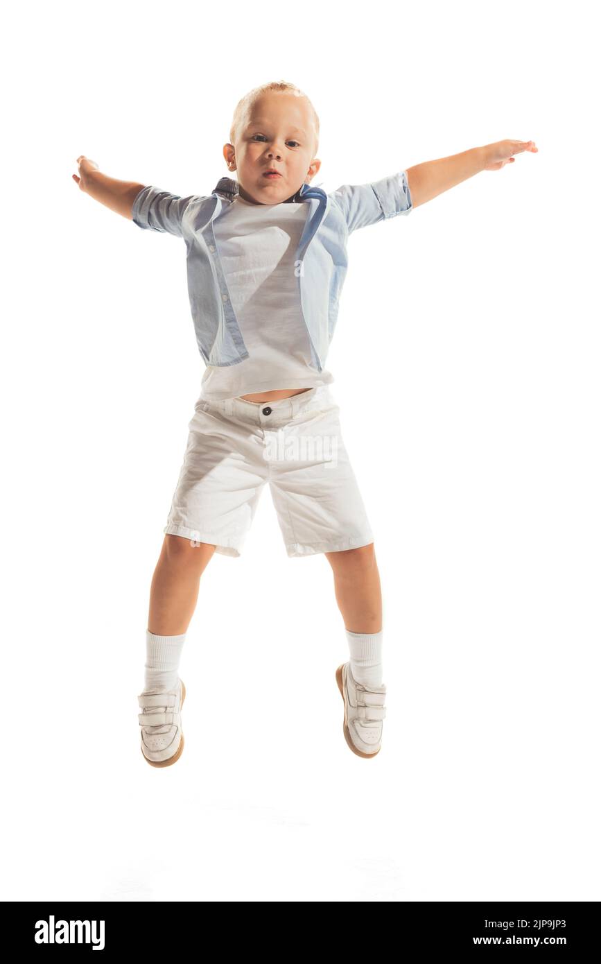 Portrait of little boy, child in casual outfit posing isolated over white studio background. Cheerfully jumping, playing Stock Photo