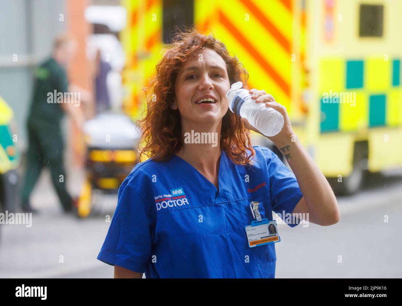 An NHS doctor cools off with a drink of water during a break at a London Hospital. The NHS is under pressure with underfunding and work pressure. Stock Photo