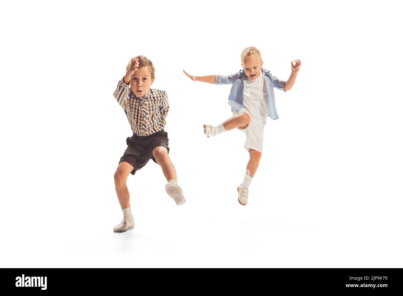 Portrait of two little boys, children playing together, running, jumping isolated over white studio background Stock Photo