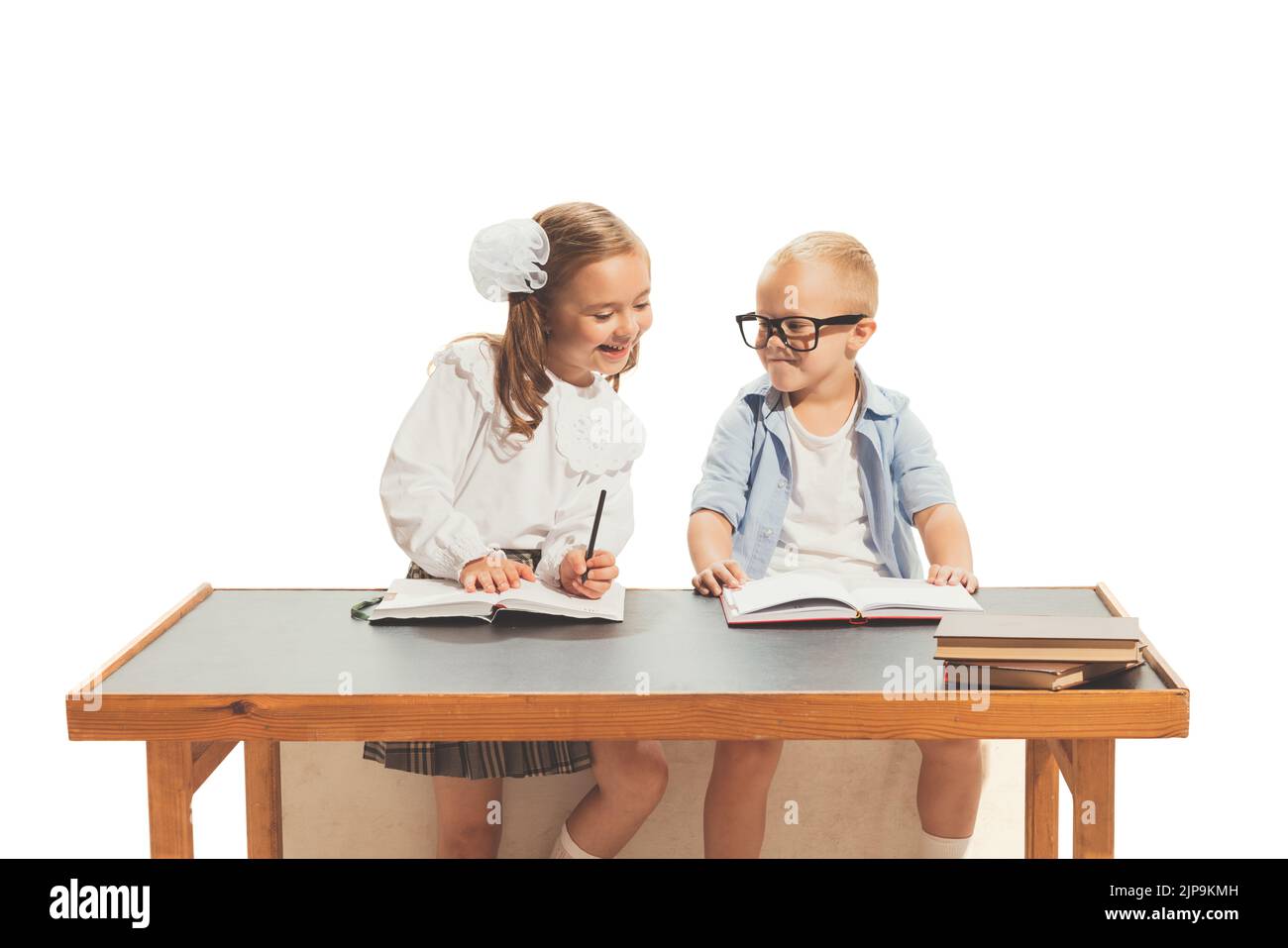 Portrait of little boy and girl, children sitting at desk and studying, doing homework isolated over white background Stock Photo