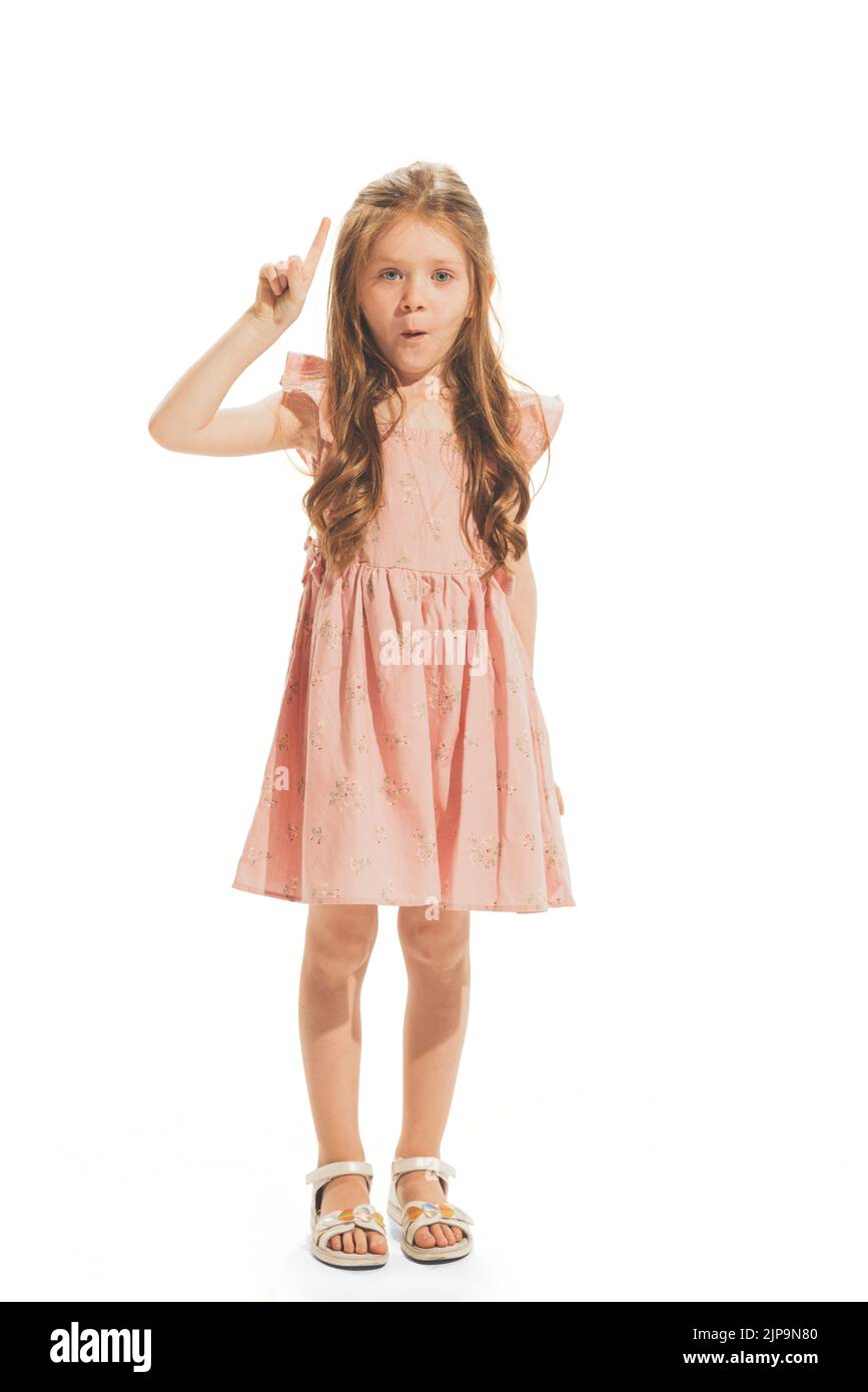 Portrait of beautiful little girl in stylish dress posing, raising finger up isolated over white studio background Stock Photo
