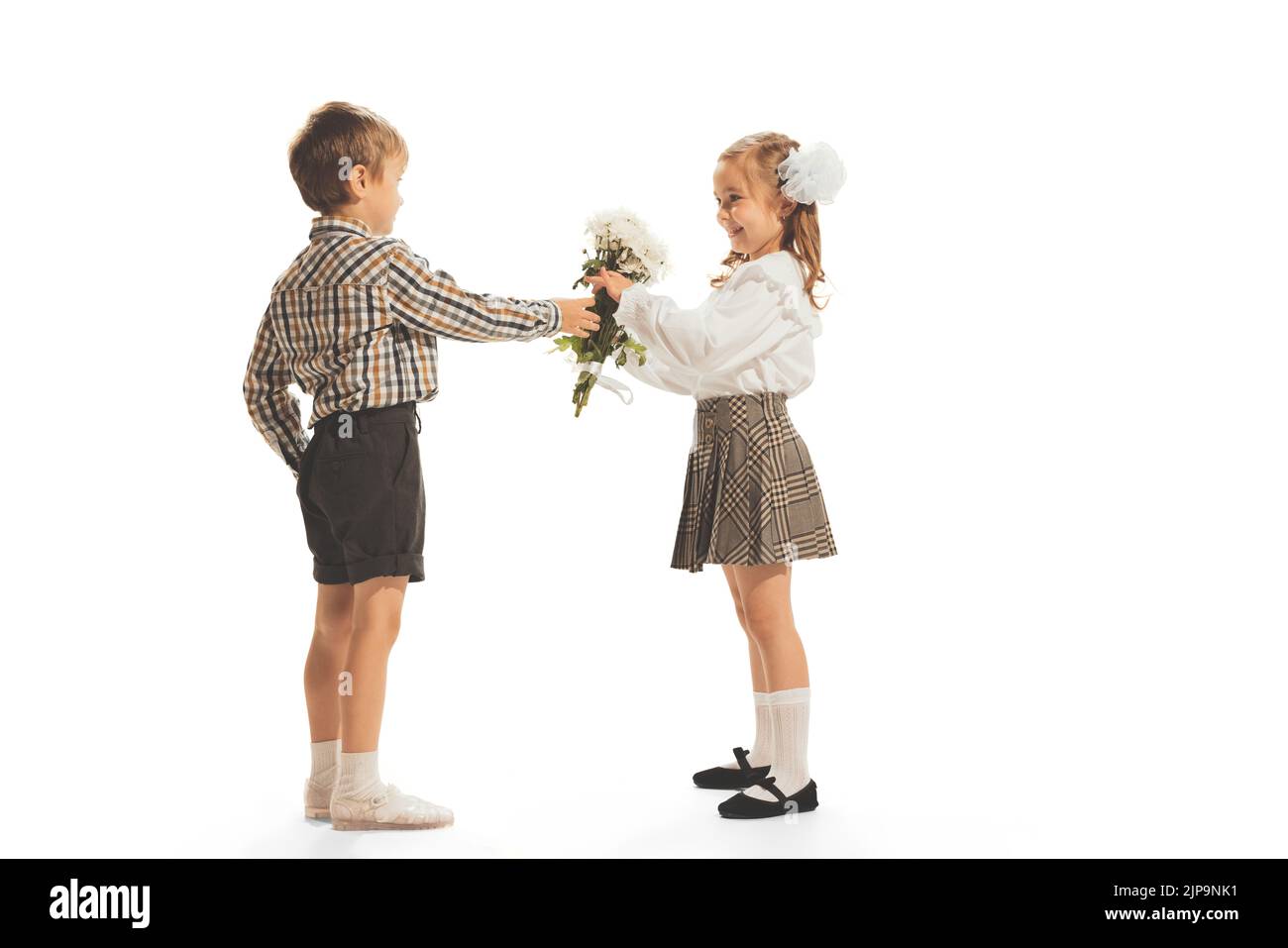 Portrait of children, boy giving girl flowers isolated over white studio background. Retro fashion Stock Photo