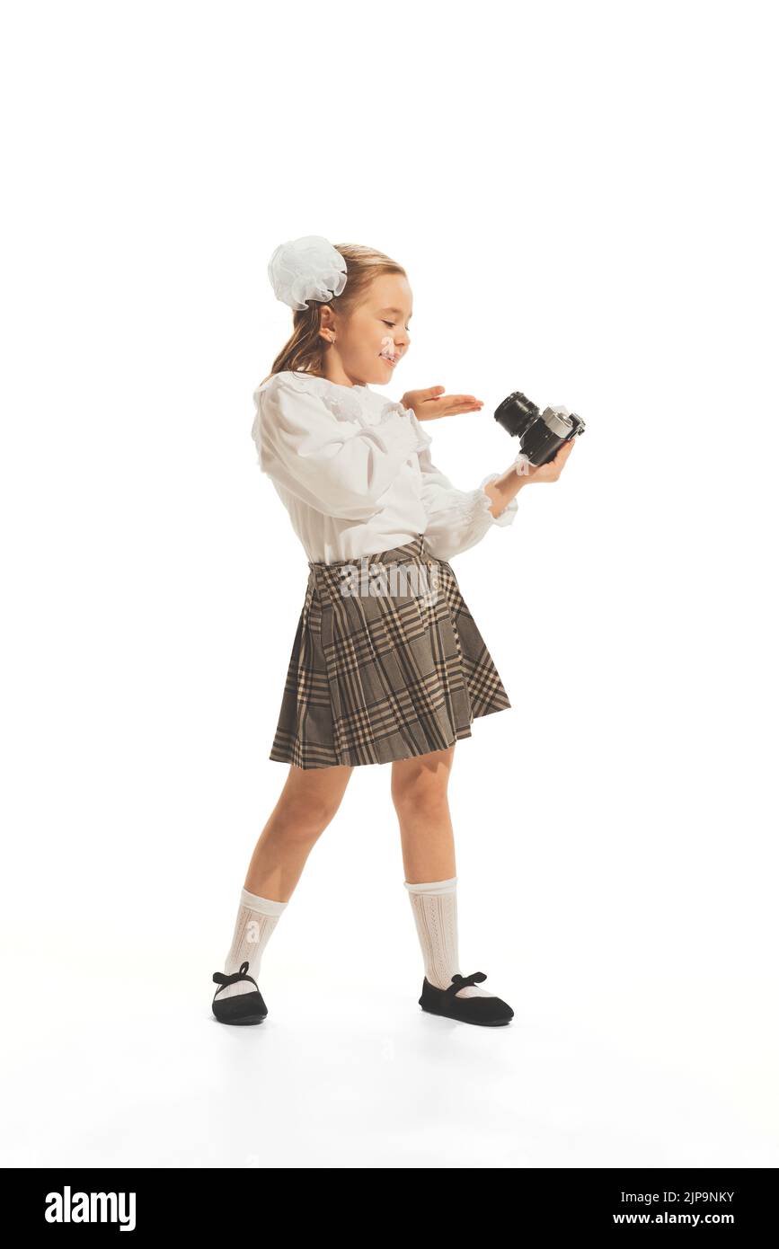 Portrait of little girl, child in school uniform with bow posing with retro camera isolated over white studio background Stock Photo