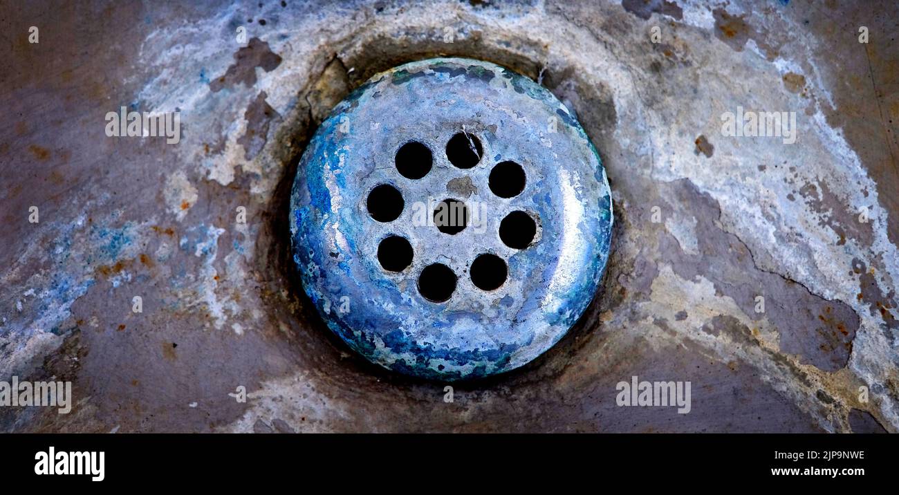 Old worn drain in sink or tub with mineral deposits and stains around