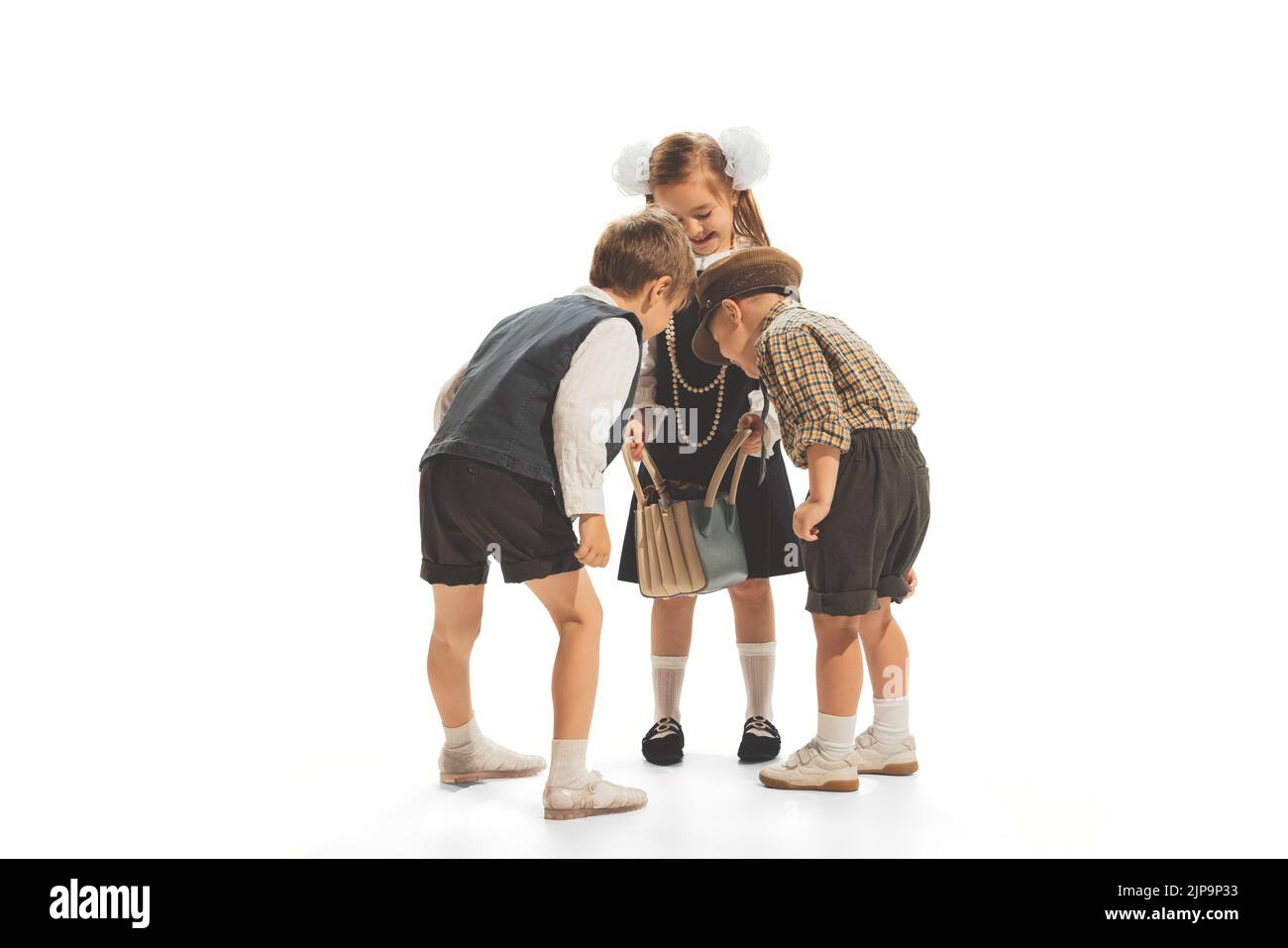 Portrait of three children, boys and girl in retro school clothes looking inside bag isolated over white studio background Stock Photo