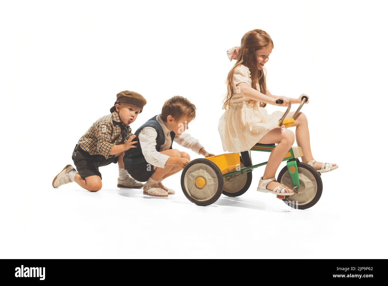 Portrait of three children, boys pulling bike with riding girl, playing together isolated over white studio background Stock Photo