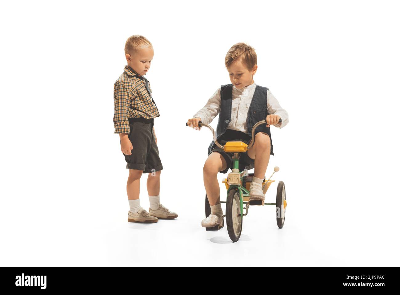 Portrait of children, boys in vintage outfits playing together, having fun, riding small bike isolated over white background Stock Photo