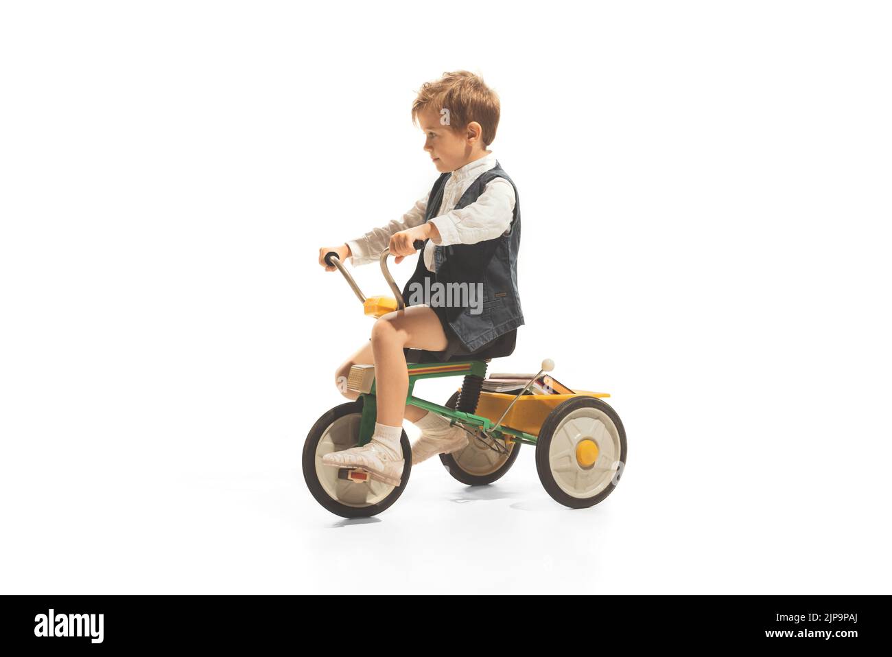 Portrait of child, boy in vintage outfit playing, having fun, riding small bike isolated over white background Stock Photo