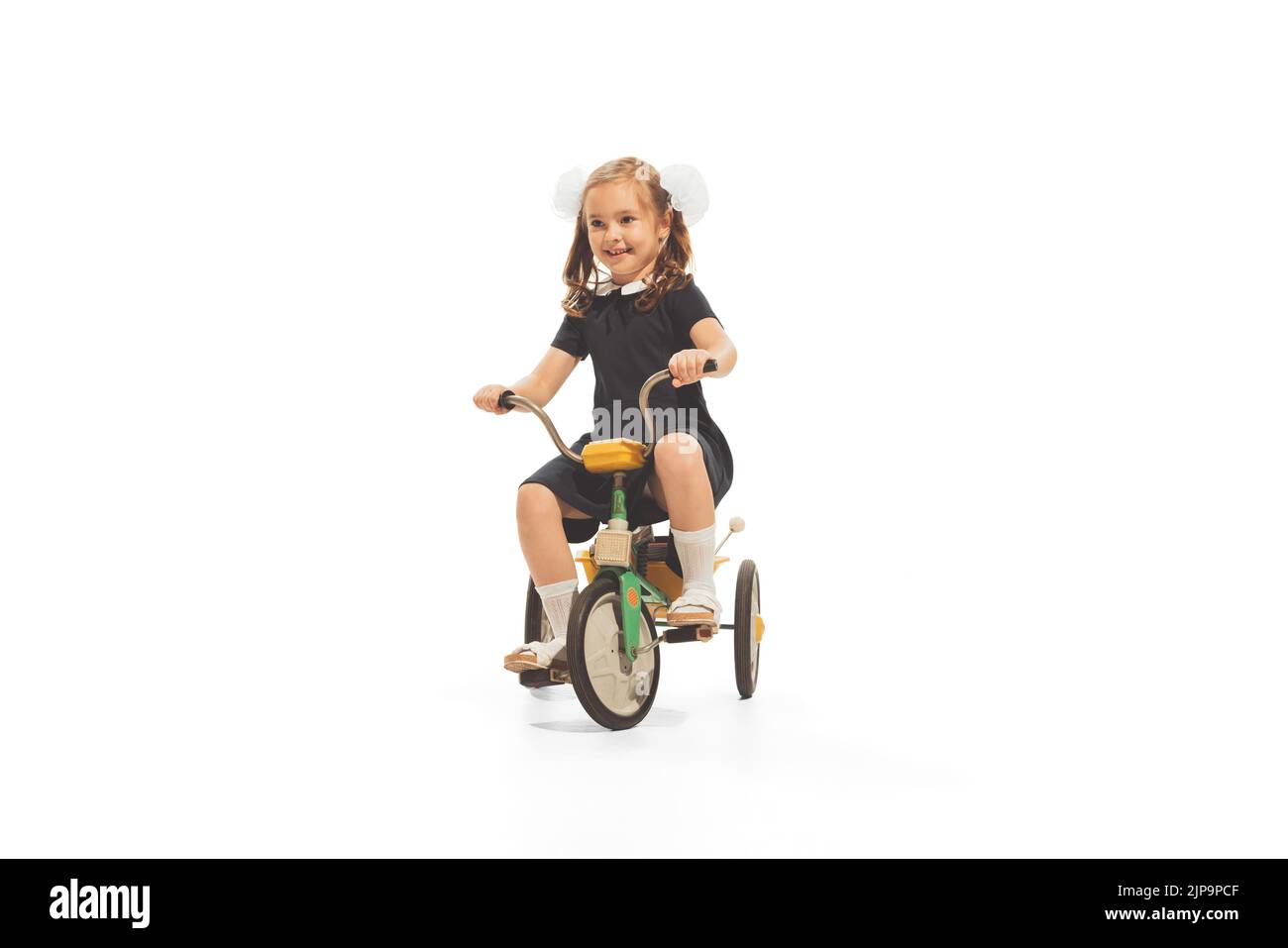 Portrait of child, girl in stylish retro dress playing, having fun, riding small bike isolated over white background Stock Photo