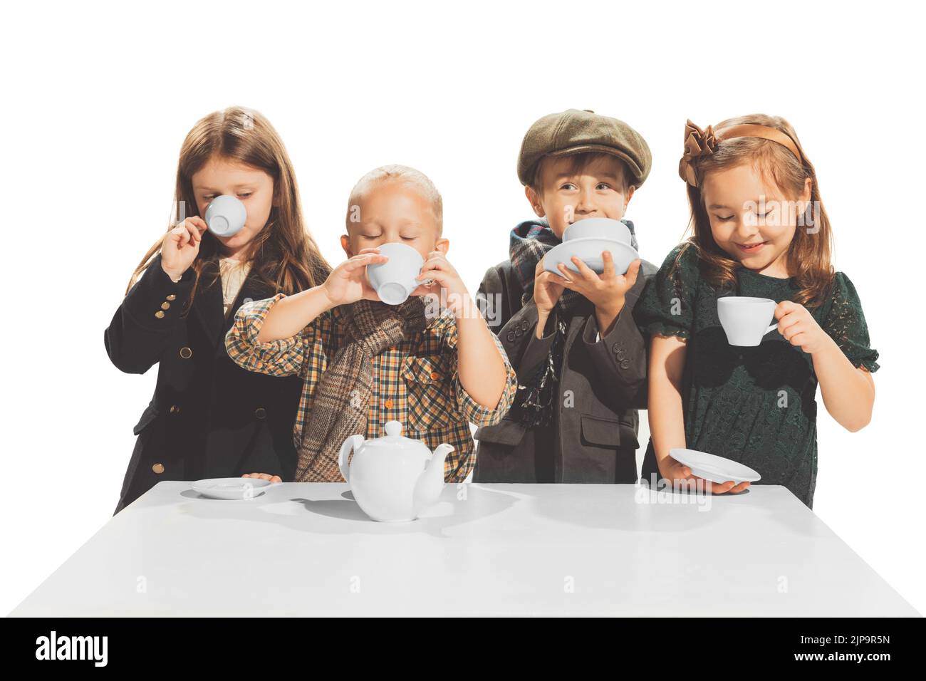 Portrait of beautiful children, boys and girls in stylish autumn clothes drinking tea, posing isolated over white studio background Stock Photo