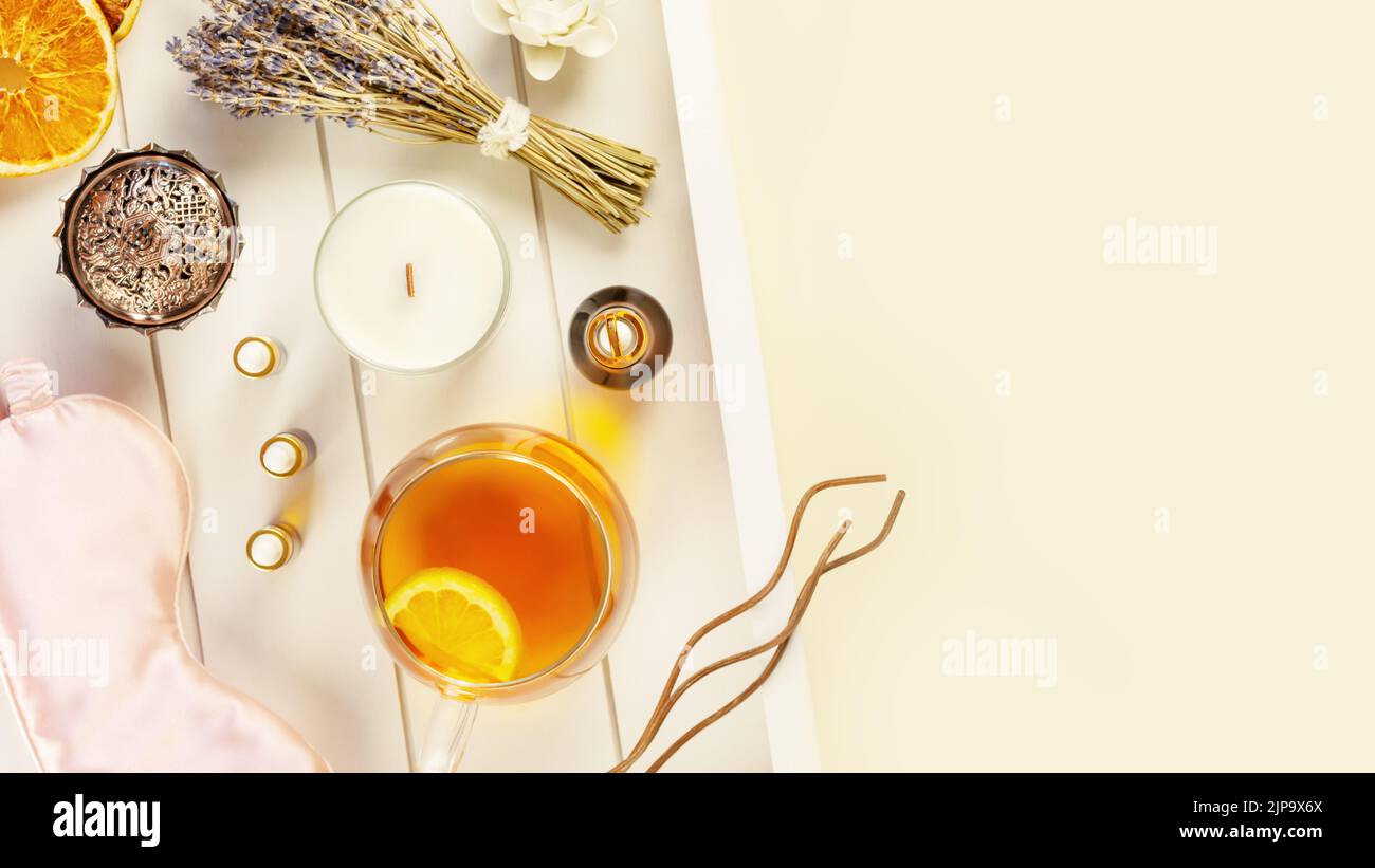 Relax at home. Cup of herbal tea, aroma candle, sticks, lavender flowers, dry oranges and natural oils on wooden tray with copy space. Insomnia or dep Stock Photo