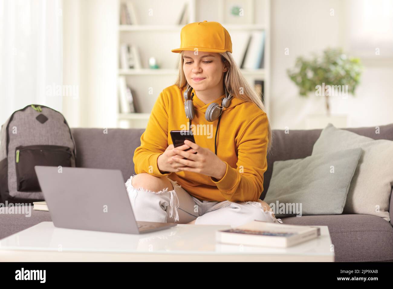 Young female sitting in front of a laptop computer at home and using a smartphone Stock Photo